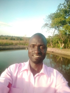 Daniel Oloya taking a seflie with a fish pond in the background